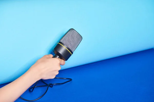 Cropped view of woman holding microphone on turquoise background — Stock Photo
