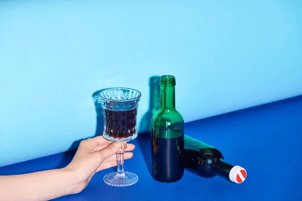 Vista recortada de la mujer sosteniendo vidrio con vino sobre fondo colorido - foto de stock