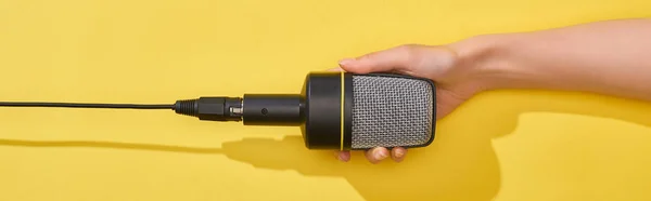 Panoramic shot of woman holding microphone on yellow background — Stock Photo