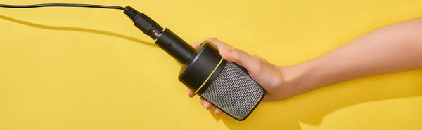 Panoramic shot of woman holding microphone on yellow background — Stock Photo