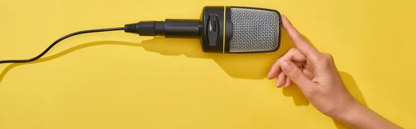 Panoramic shot of woman holding microphone on yellow background — Stock Photo