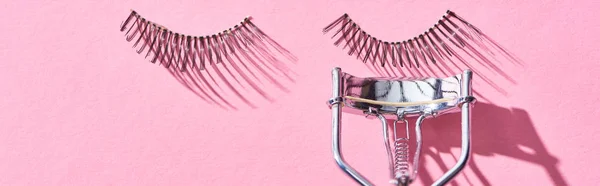 Panoramic shot of false eyelashes and eyelash curler on pink background — Stock Photo