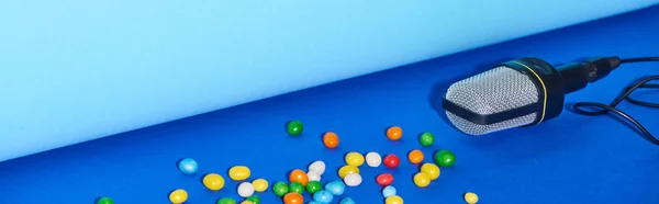 Tiro panorâmico de microfone preto com doces no fundo colorido — Fotografia de Stock
