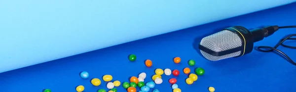 Panoramic shot of black microphone with candies on colorful background — Stock Photo