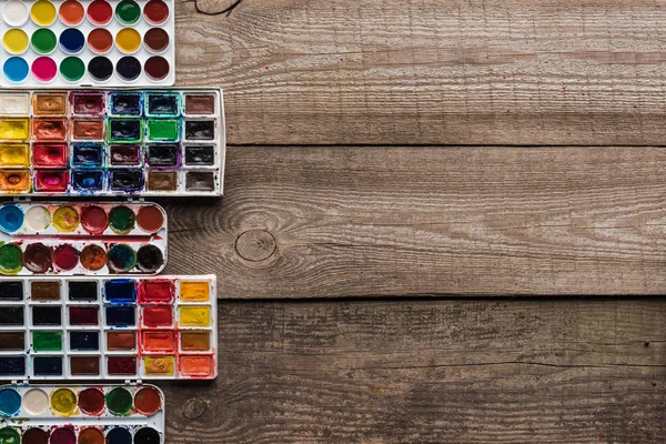 Vista superior de paletas de pintura de colores en la superficie marrón de madera con espacio de copia - foto de stock