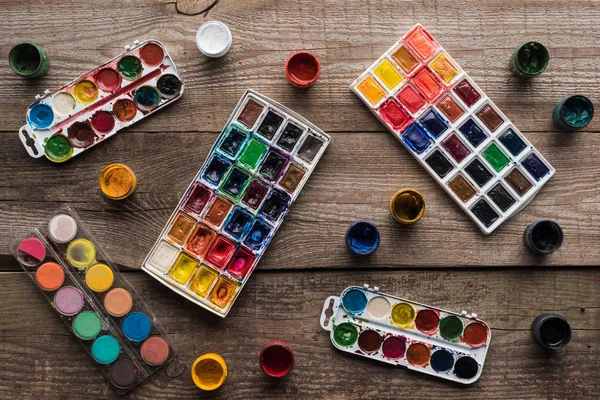 Top view of colorful paint palettes on wooden brown surface with gouache — Stock Photo