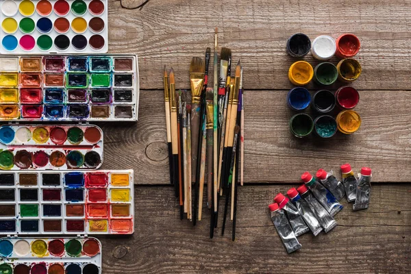 Vue de dessus de diverses peintures sur surface marron bois avec pinceaux — Photo de stock