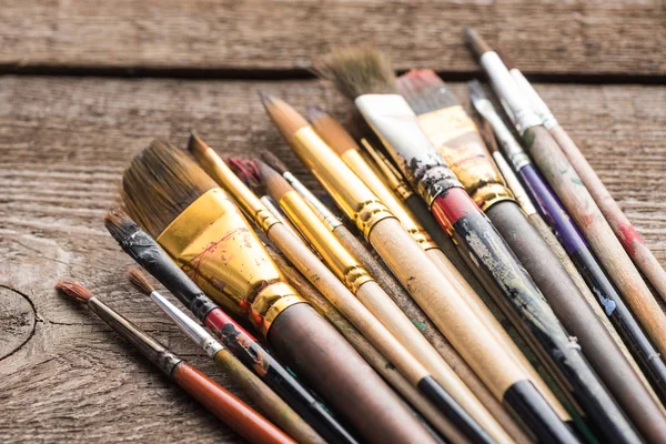 Close up view of aged paintbrushes on wooden brown surface — Stock Photo