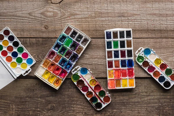 Vue de dessus des palettes de peinture à l'aquarelle sur la surface brun bois — Photo de stock