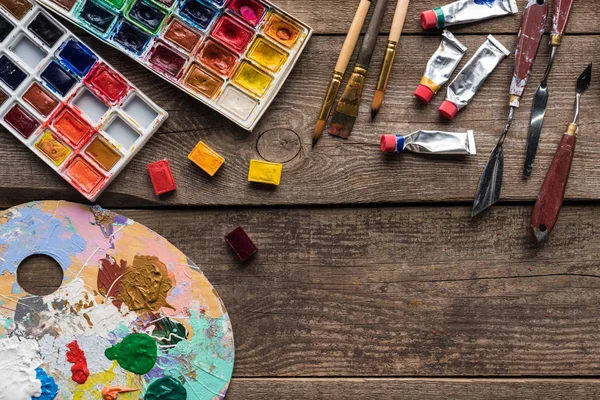 Vue de dessus des palettes de peinture et des outils de dessin sur la surface en bois avec espace de copie — Photo de stock