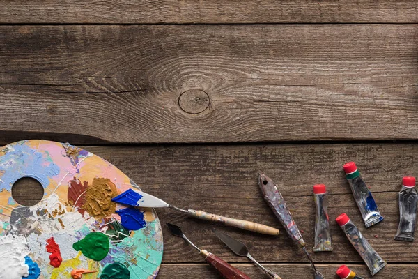 Top view of palette with multicolored oil paints and drawing tools on wooden surface with copy space — Stock Photo