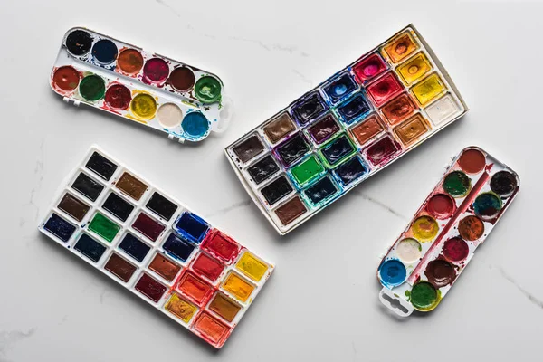 Vista superior de coloridas paletas de pintura sobre la superficie blanca de mármol - foto de stock