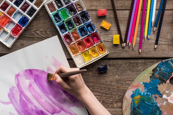 Vue recadrée du dessin d'artiste dans le carnet de croquis avec des peintures à l'aquarelle à la table en bois — Photo de stock