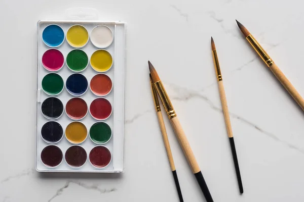 Vista dall'alto della tavolozza di colori ad acquerello e pennelli sulla superficie di marmo bianco — Foto stock
