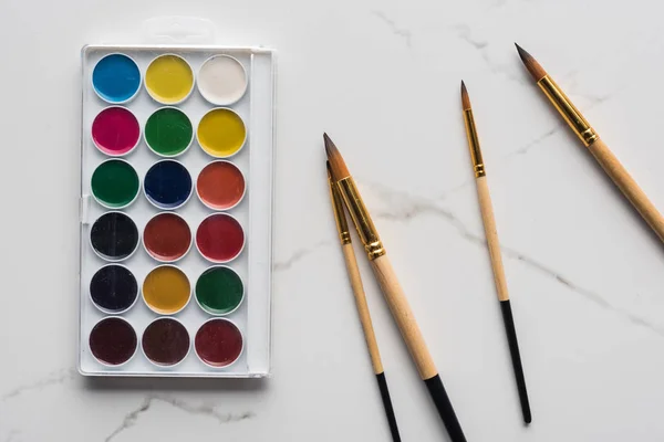 Vue de dessus de la palette de peinture aquarelle et des pinceaux sur la surface en marbre blanc — Photo de stock