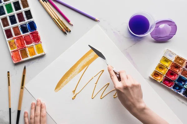 Vue partielle du dessin avec spatule sur papier blanc près des pinceaux sur la surface en marbre blanc — Photo de stock