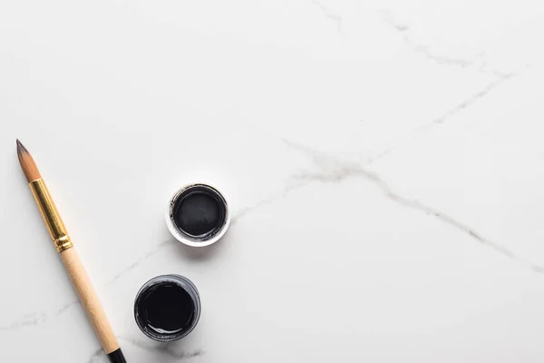 Top view of black gouache paint and paintbrush on marble white surface with copy space — Stock Photo