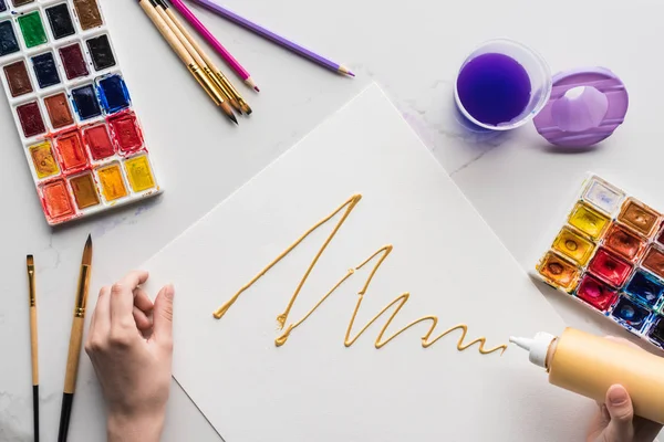 Vue recadrée du dessin de l'artiste avec la peinture de la bouteille sur papier blanc sur la surface de marbre blanc — Photo de stock