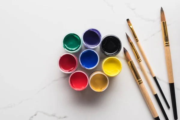 Top view of multicolored gouache paints and paintbrushes on marble white surface — Stock Photo