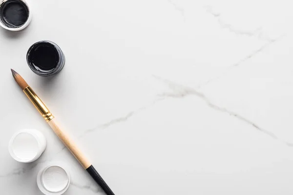 Top view of black and white paints near paintbrush on marble white surface — Stock Photo