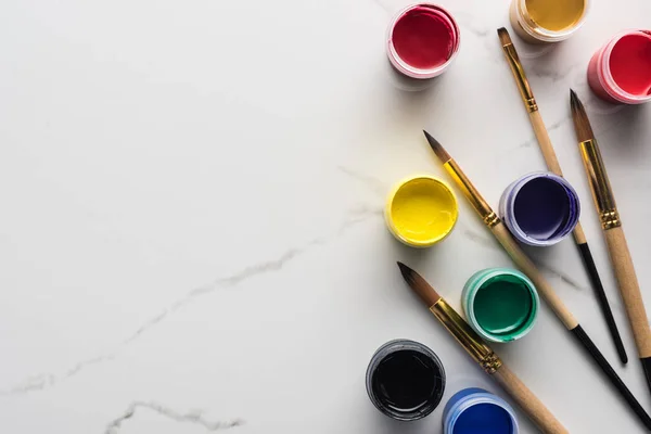 Top view of multicolored gouache paints and paintbrushes on marble white surface with copy space — Stock Photo