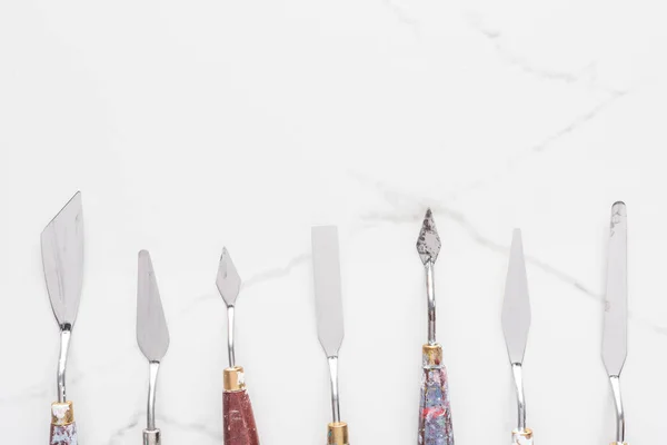 Flat lay with metal spatulas for drawing on marble white surface with copy space — Stock Photo