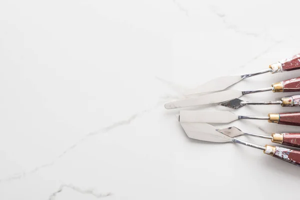 Top view of metal spatulas for drawing on marble white surface with copy space — Stock Photo