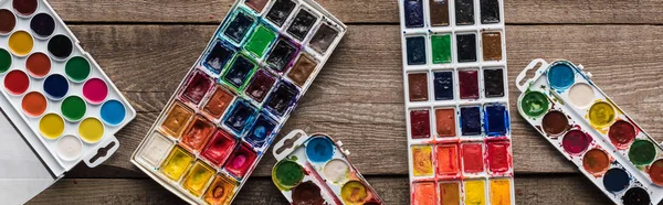 Top view of colorful paint palettes on wooden brown surface with gouache, panoramic shot — Stock Photo