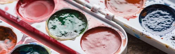 Vista de cerca de las paletas de pintura acuarela en la mesa de madera, plano panorámico - foto de stock