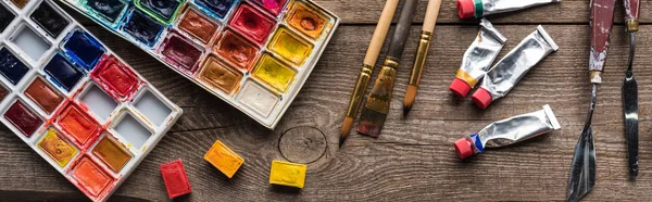 Vista superior de coloridas paletas de pintura y herramientas de dibujo en la superficie de madera, plano panorámico - foto de stock