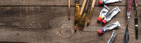 Vista dall'alto di pitture ad olio in tubi, pennelli e spatole su superficie in legno con spazio copia, scatto panoramico — Foto stock
