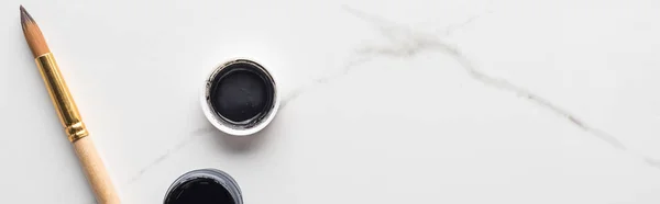 Top view of black gouache paint and paintbrush on marble white surface with copy space, panoramic shot — Stock Photo
