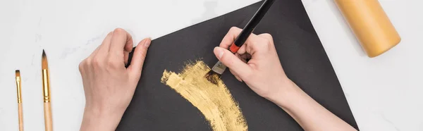 Ausgeschnittene Ansicht der Zeichnung des Künstlers mit goldener Farbe in schwarzem Papier auf Marmoroberfläche, Panoramaaufnahme — Stockfoto