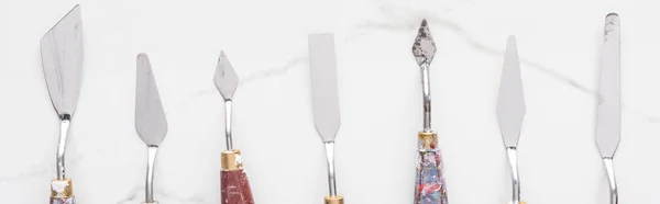 Flat lay with metal spatulas for drawing on marble white surface, panoramic shot — Stock Photo