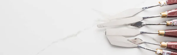 Vista superior de espátulas de metal para desenho na superfície branca de mármore com espaço de cópia, tiro panorâmico — Fotografia de Stock