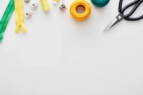 Vista superior de tesouras, bolas de fios de tricô, zíperes, fios, dedal e bobinas no fundo branco — Fotografia de Stock