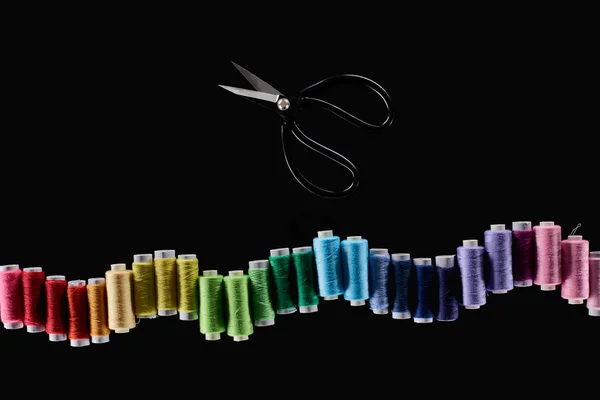 Vista superior de hilos brillantes y coloridos y tijeras aisladas en negro - foto de stock