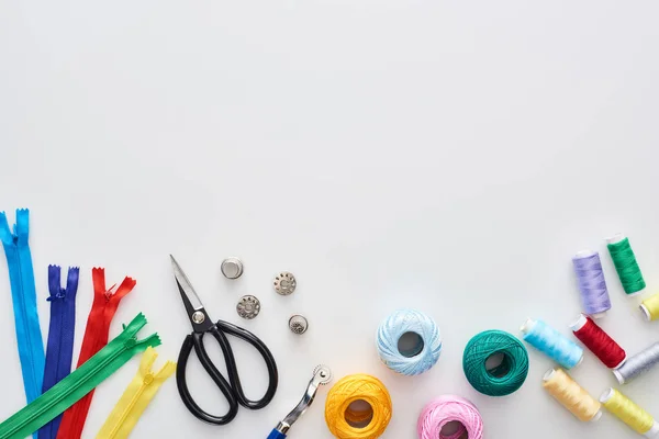 Vista superior de zíperes, tesouras, dedais, fios, bolas de fios de tricô, bobinas, roda de rastreamento no fundo branco — Fotografia de Stock