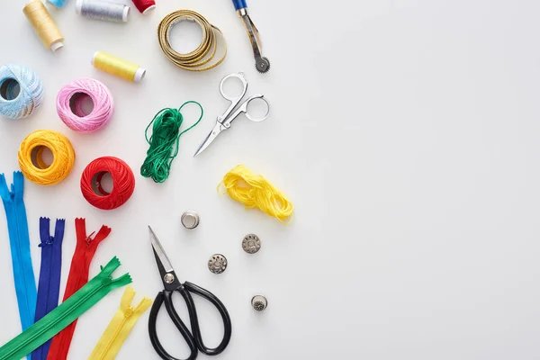 Top view of zippers, scissors, thimbles, threads, knitting yarn balls, bobbins, tracing wheel, measuring tape on white background — Stock Photo