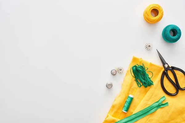 Top view of zipper, scissors, thimbles, threads, knitting yarn balls, bobbins, fabric on white background — Stock Photo