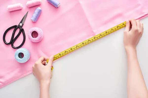 Cropped view of seamstress measuring fabric with measuring tape on white background — Stock Photo