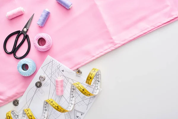 Ansicht von Stoff, Strickgarnbällchen, Schnittmuster, Scheren, Fingerhüte, Spulen, Maßband und Fäden auf weißem Hintergrund — Stockfoto