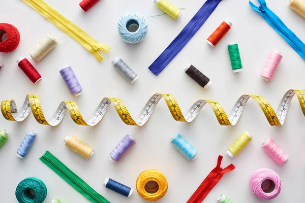 Top view of measuring tape, colorful threads and zippers on white background — Stock Photo