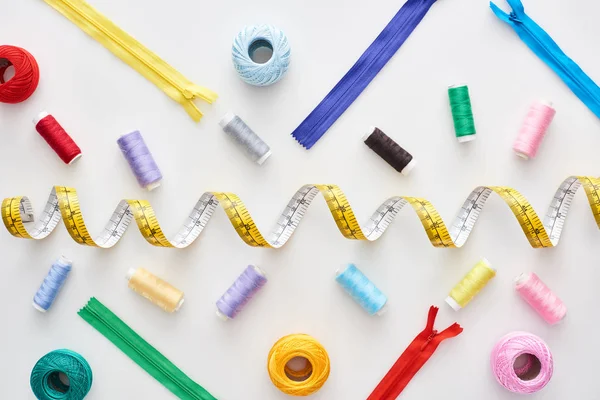 Top view of measuring tape, colorful threads and zippers on white background — Stock Photo