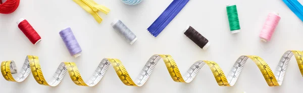 Top view of measuring tape, colorful threads and zippers on white background — Stock Photo