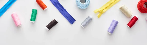 Panoramic shot of colorful threads, knitting yarn balls and zippers on white background — Stock Photo