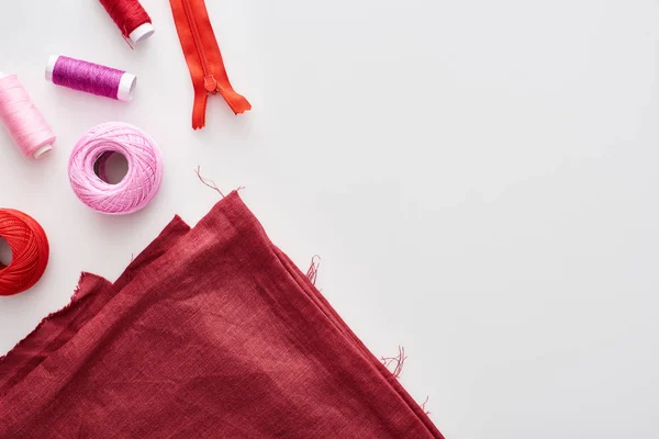 Draufsicht auf bunte Fäden, Strickgarnknäuel, Stoff und Reißverschlüsse auf weißem Hintergrund — Stockfoto