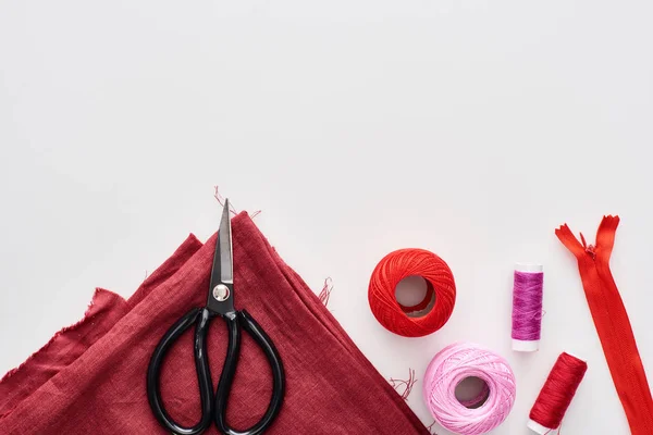 Draufsicht auf bunte Fäden, Strickgarnknäuel, Stoff, Schere und Reißverschluss auf weißem Hintergrund — Stockfoto