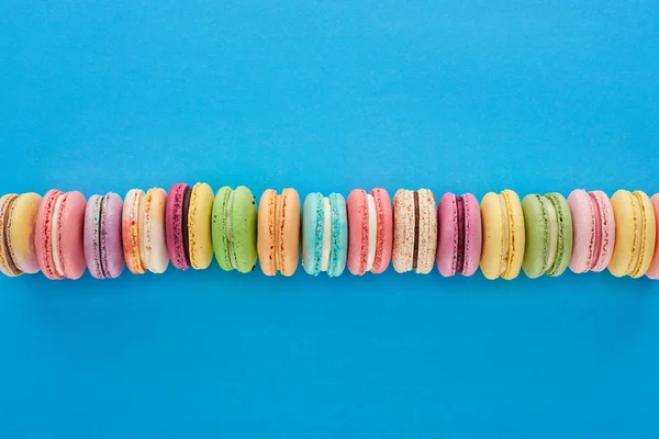 Top view of multicolored delicious French macaroons in row on blue bright background — Stock Photo