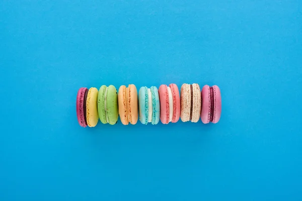 Top view of multicolored delicious French macaroons in line on blue bright background — Stock Photo